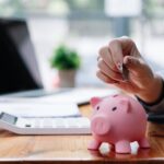 Close up hand of woman putting money coin into pink piggy bank for saving money wealth and