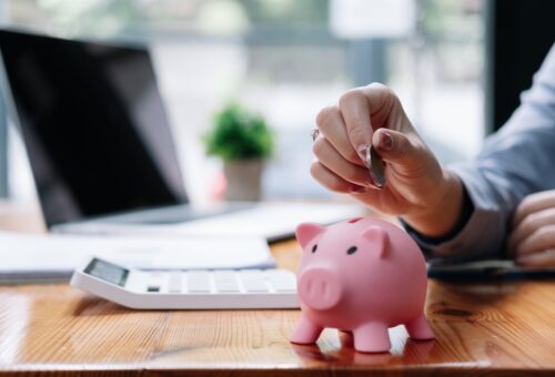 Close up hand of woman putting money coin into pink piggy bank for saving money wealth and