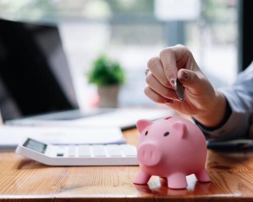 Close up hand of woman putting money coin into pink piggy bank for saving money wealth and