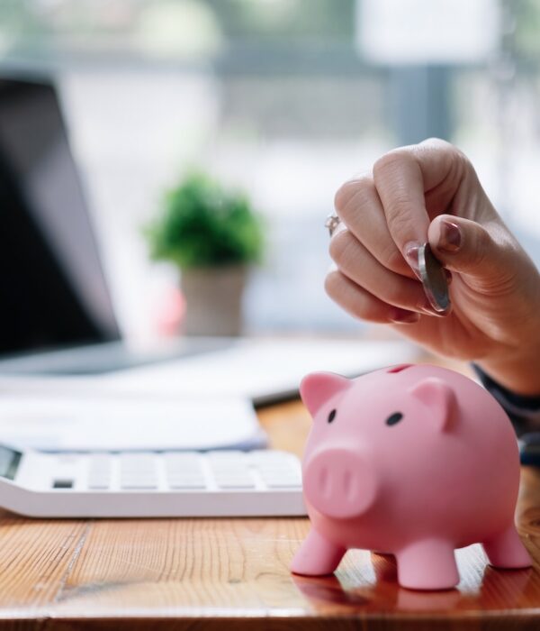 Close up hand of woman putting money coin into pink piggy bank for saving money wealth and