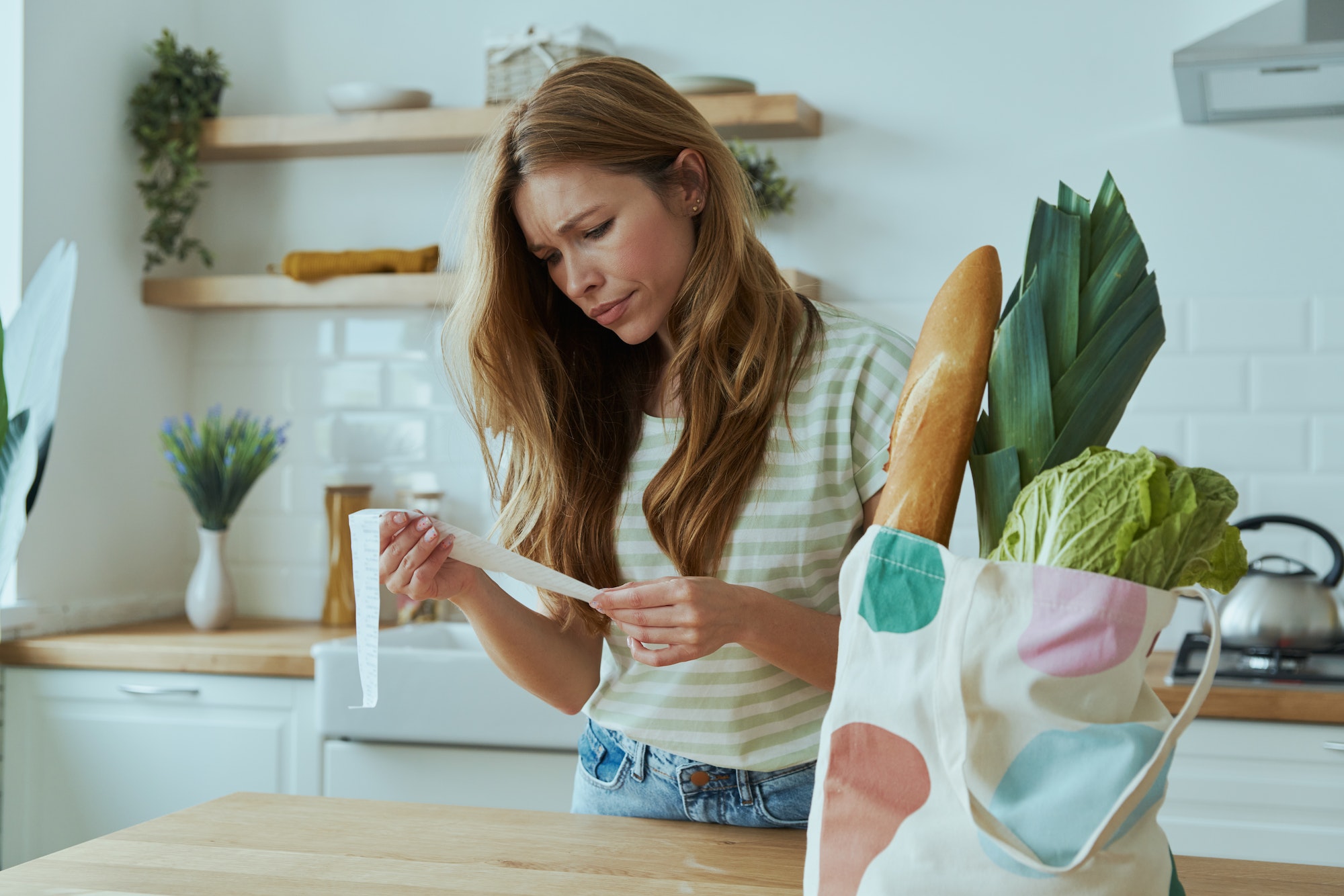 Displeased young woman checking receipts while standing at the domestic kitchen