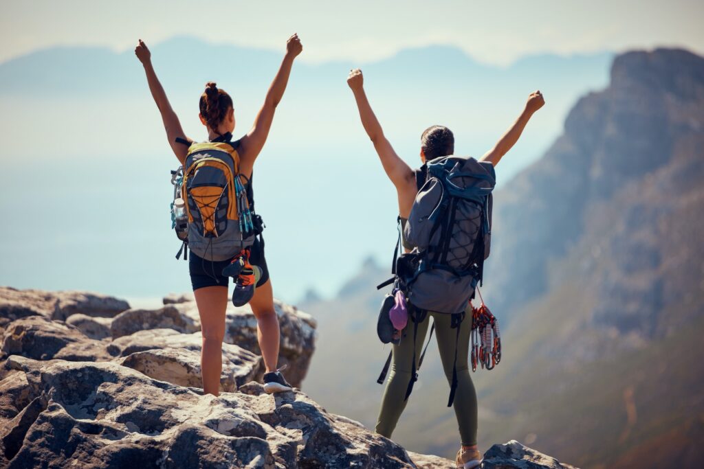 Hiking, mountain top and backpack women celebrate success, motivation and winning cliff climbing or